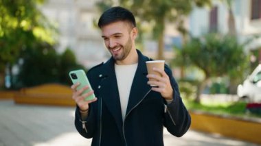 Genç İspanyol adam akıllı telefon kullanıp parkta kahve içiyor.