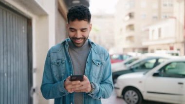 Genç Arap adam sokakta akıllı telefon kullanarak kendinden emin gülümsüyor.