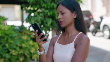 Genç ve güzel bir kadın sokakta endişeli bir ifadeyle akıllı telefondan konuşuyor.