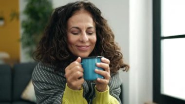 Orta yaşlı İspanyol kadın caddede kanepede kahve içiyor.