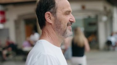 Orta yaşlı bir adam sokakta kendine güvenerek gülümsüyor.
