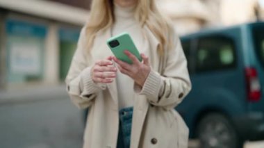Sokakta akıllı telefon kullanan, kendine güvenen genç sarışın kadın.