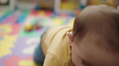 Adorable hispanic baby playing with car toy sitting on floor at kindergarten