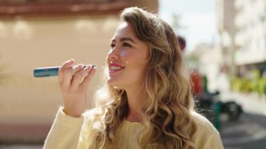 Genç sarışın kadın gülümsüyor. Kendine güveni tam. Akıllı telefondan konuşuyor.