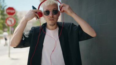 Genç, beyaz bir adam, kendinden emin bir şekilde gülümsüyor müzik dinliyor ve sokakta dans ediyor.