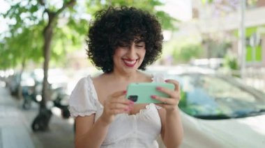 Young middle east woman smiling confident watching video on smartphone at street