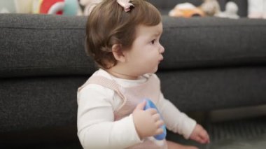 Sevimli bebek evde yerde oturan plastik halkayı ısırıyor.