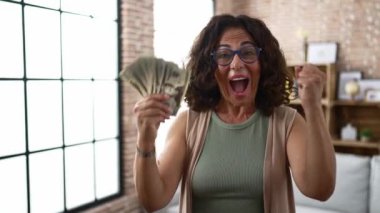 Middle age hispanic woman holding dollars banknotes