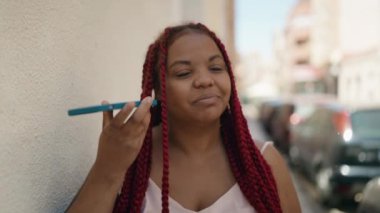 Afro-Amerikalı kadın gülümsüyor. Caddedeki akıllı telefondan kendine güvenen sesli mesaj dinliyor.