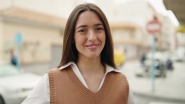 Young hispanic woman smiling confident doing ok sign with thumb up at street