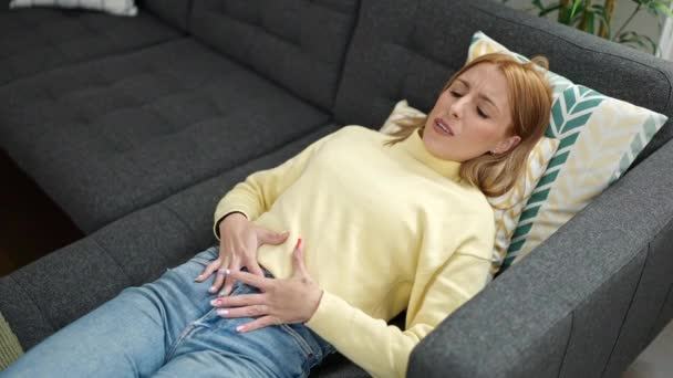 Young Blonde Woman Suffering Menstrual Pain Lying Sofa Home — 图库视频影像