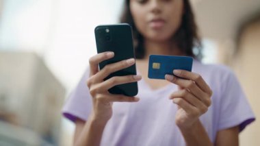 Young african american woman using smartphone and credit card at street