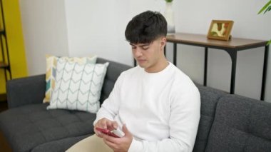 Evdeki kanepede oturan Latin asıllı genç bir adam.