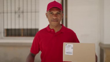 Young latin man delivery worker holding package doig ok gesture with finger at street