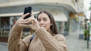 Genç, güzel, İspanyol bir kadın akıllı telefonuyla caddede video kaydediyor.