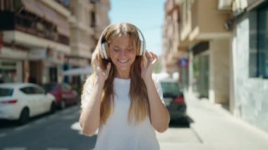 Young blonde girl smiling confident listening to music and dancing at street