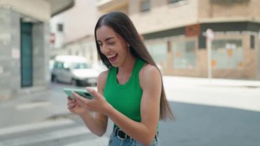 Genç ve güzel İspanyol kadın gülümsüyor. Sokakta akıllı telefondan videolar izliyor.