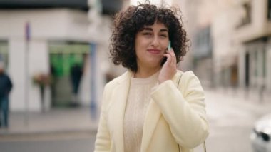 Gülümseyen genç bir kadın caddedeki akıllı telefondan konuşuyor.