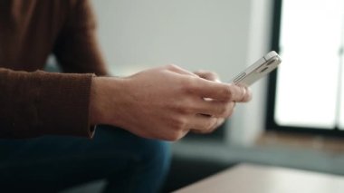 Evdeki kanepede oturan, akıllı telefon kullanan genç bir İspanyol.