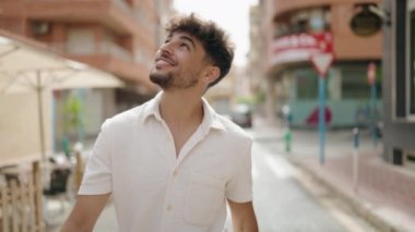 Genç Arap adam sokakta yürürken kendinden emin gülümsüyor.