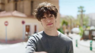 Genç İspanyol adam gülümsüyor. Kendinden emin. Sokakta el kol hareketi yapıyor.