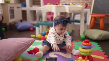 Öğretmen ve anaokulu öğrencileri anaokulunda yerde oturmuş oyuncaklarla oynuyorlar.