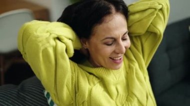 Orta yaşlı İspanyol kadın, elleri başının üstünde, caddede kanepede oturuyor.