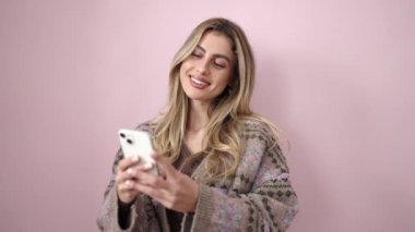 Young blonde woman smiling confident using smartphone over isolated pink background