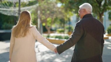 Orta yaşlı çift parkta el ele yürüyor.