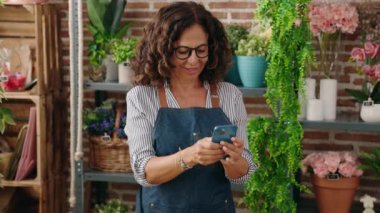 Middle age woman florist smiling confident using smartphone at flower shop