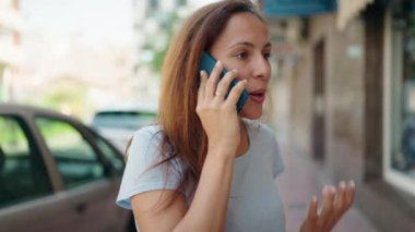 Gülümseyen genç bir kadın caddedeki akıllı telefondan konuşuyor.