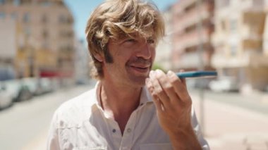 Genç adam gülümsüyor. Kendine güveniyor. Sokakta akıllı telefondan konuşuyor.