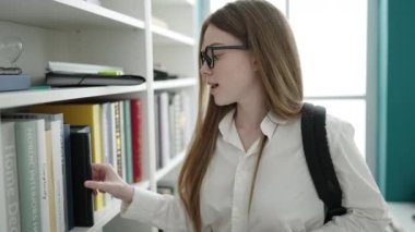 Üniversite sınıfında akıllı telefon kullanarak kitap arayan genç sarışın kız öğrenci.