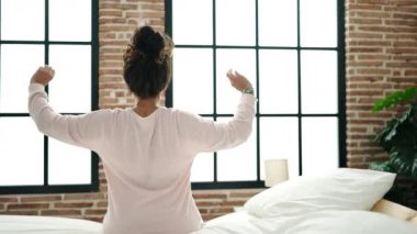 Middle age hispanic woman waking up stretching arms at bedroom