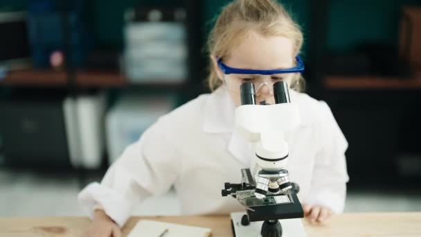 Adorable Blonde Girl Student Using Microscope Writing Notebook Laboratory Classroom — Video