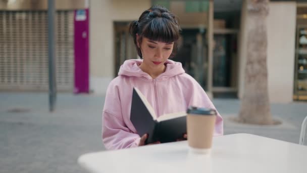 年轻的惊慌失措的女人带着自信的笑容在咖啡店的阳台上看书 — 图库视频影像