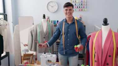 Young hispanic man tailor smiling confident holding scissors and thread at clothing factory