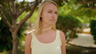 Parkta duran rahat yüzlü genç sarışın kadın.