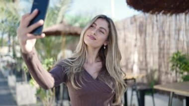 Genç sarışın kadın, kahve dükkanının terasında kendinden emin bir şekilde selfie çekiyor.