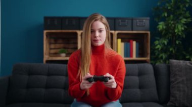 Young blonde woman playing video game sitting on sofa at home