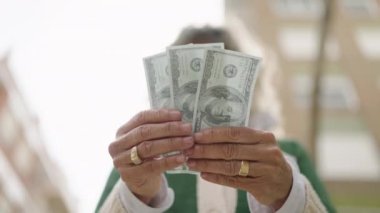 Orta yaşlı kadın gülümsüyor. Sokakta dolarları sayıyor.