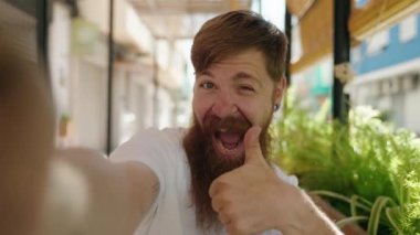 Genç kızıl saçlı adam kahve dükkanının terasında masanın üzerinde kameranın önünde selfie çekiyor.