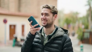 Genç adam gülümsüyor. Kendine güveniyor. Sokakta akıllı telefondan konuşuyor.