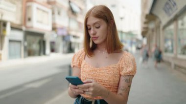 Young redhead woman using smartphone at street