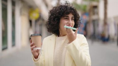 Young woman talking on the smartphone drinking coffee at street