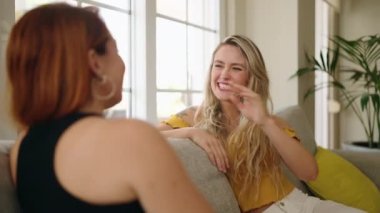 Two women sitting on sofa speaking at home