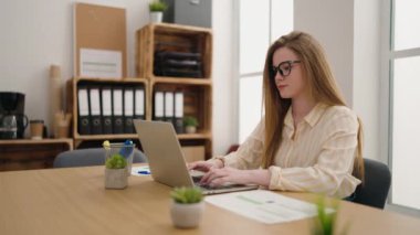 Ofiste çalışan genç sarışın iş kadını dizüstü bilgisayar kullanıyor.