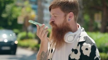 Genç kızıl saçlı adam gülümsüyor. Parktaki akıllı telefondan konuşuyor.