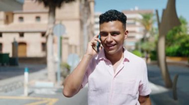 Young latin man smiling confident talking on the smartphone walking at street