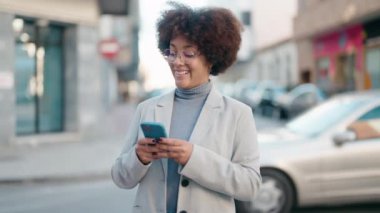 Afro-Amerikalı kadın sokakta akıllı telefon kullanarak kendine güveniyor.